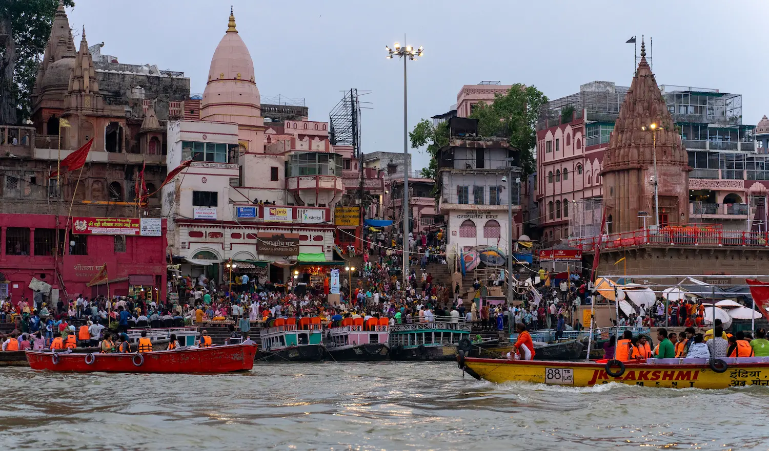 View of Dashashwamedh Ghat from the Ganga River showing temples, crowds, and passenger boats in Varanasi